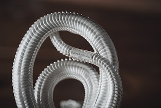 A close-up of a metallic, coil-like structure with a textured surface. The metal appears shiny and has a label reading 'COPPERIST.WU' attached to it. The background is blurred, giving emphasis to the foreground object.