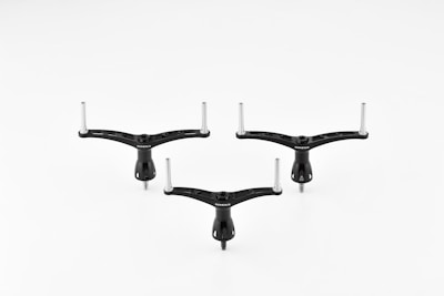 Three identical black tripod-like objects with two protruding metal rods on a white background. The objects are positioned symmetrically.
