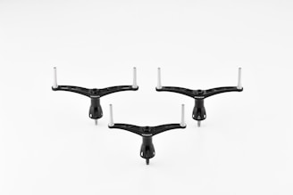 Three identical black tripod-like objects with two protruding metal rods on a white background. The objects are positioned symmetrically.