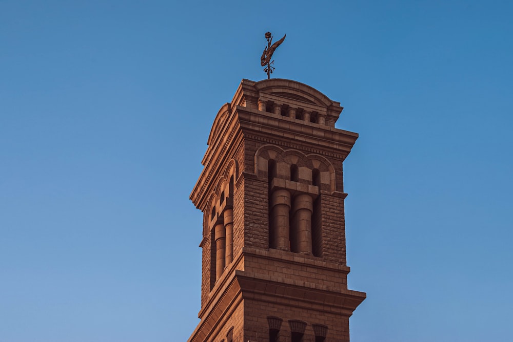 a tall brick clock tower with a weather vane on top