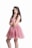 A young woman with long, wavy hair is wearing a sparkling pink dress and a jeweled tiara. She is standing with one hand on her waist and the other resting near her chin, exuding elegance.