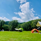A sturdy green tent pitched on a grassy campsite under a clear blue sky.