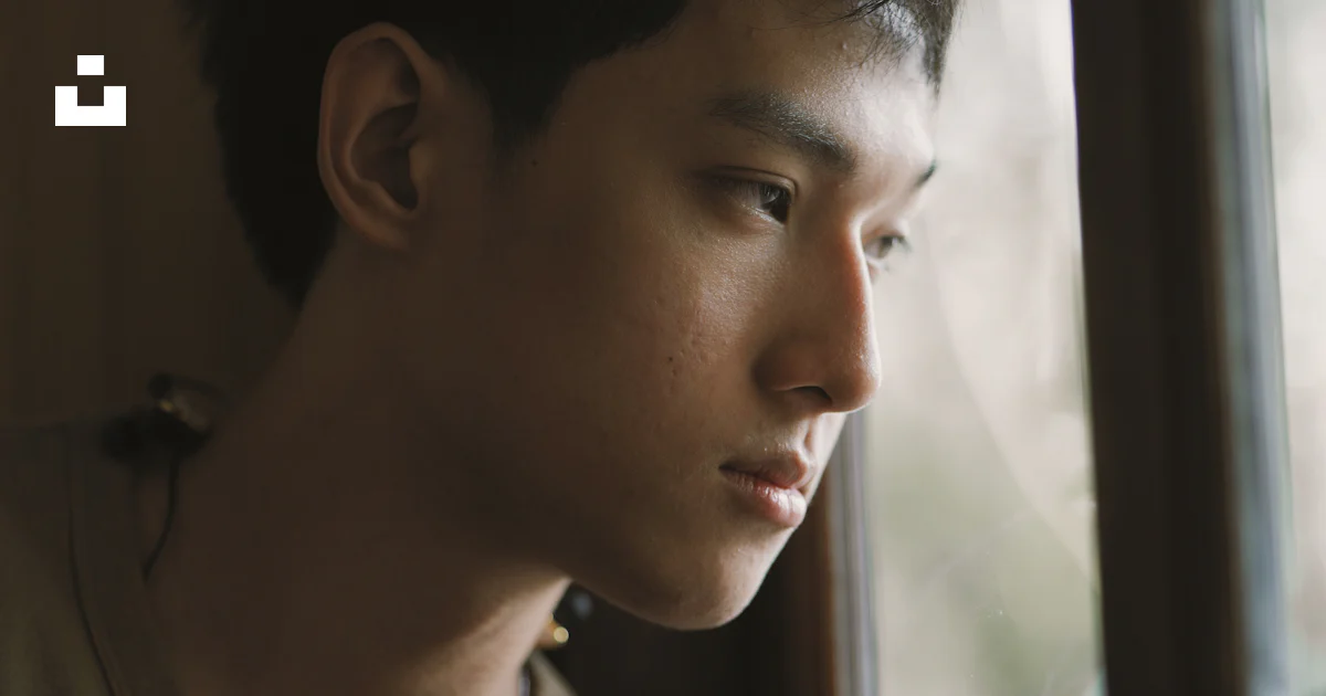 A man looking out of a window with a serious look on his face photo ...