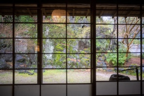 A serene Japanese-style garden courtyard viewed from a large glass window inside a modern home.