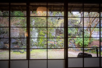 A serene Japanese-style garden courtyard viewed from a large glass window inside a modern home.