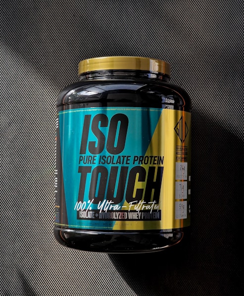 A large black container of ISO TOUCH pure isolate protein with a black and teal label, featuring bold text and nutritional information. The label includes details such as 