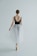 A ballet dancer is captured from behind, standing on pointe. She wears a black leotard with lace detailing on the back and a flowing white tulle skirt. Her hair is styled in a neat bun, and she is poised gracefully in a minimalist, light-filled space.