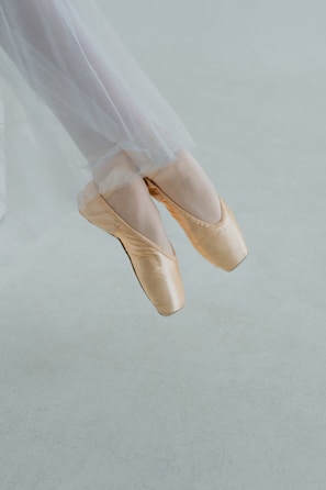Close-up of a dancer’s feet in ballet slippers poised delicately on tiptoe against a wooden floor.