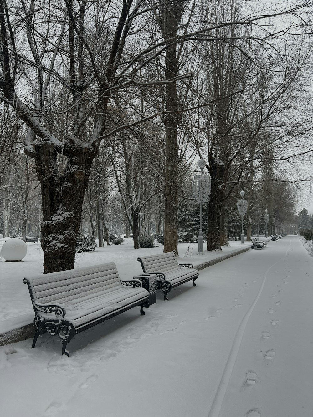 a park bench covered in snow next to a tree