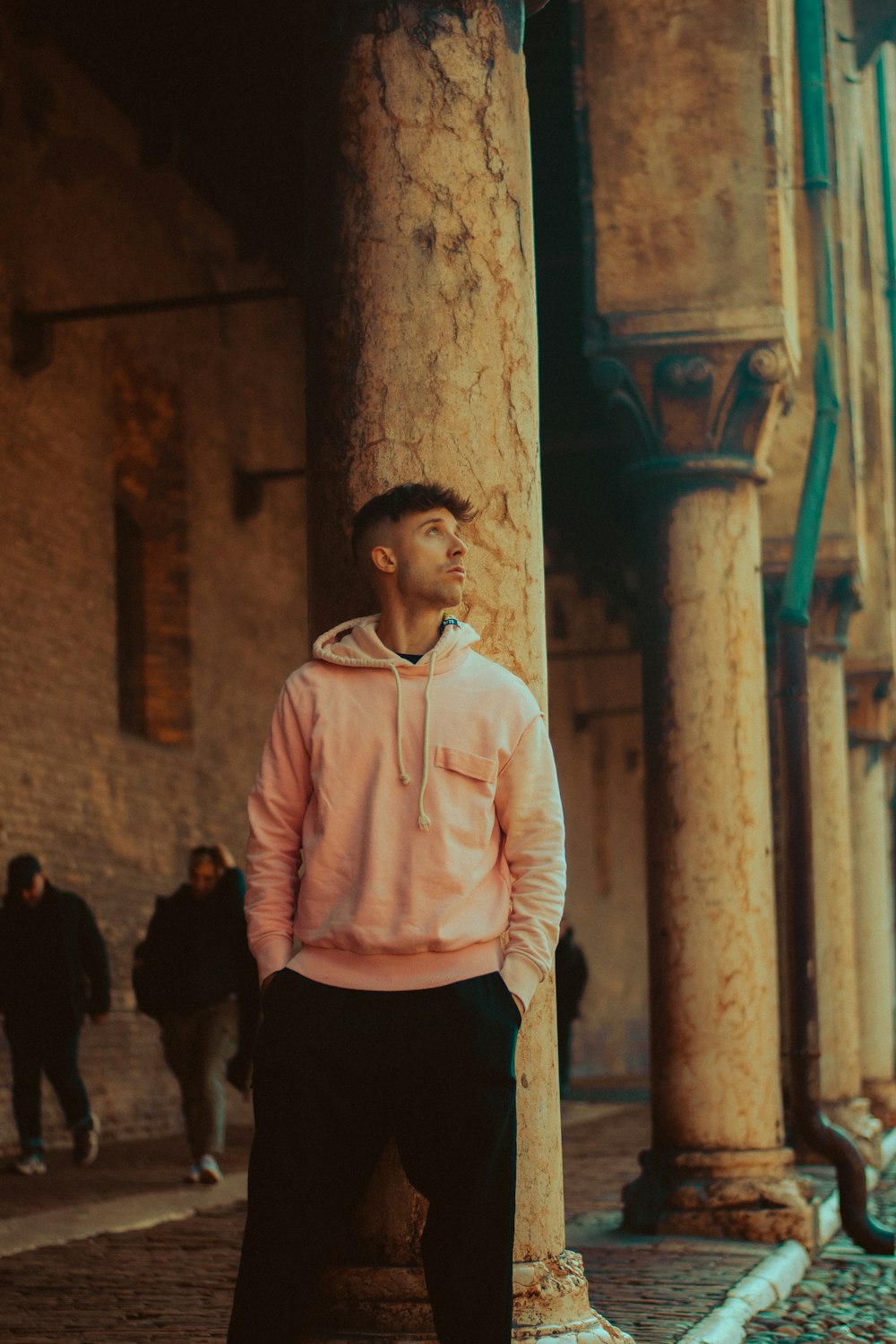 a man in a pink hoodie leaning against a pillar