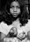 A young girl with medium-length hair is holding a few tomatoes in her hands. She has an expression of calm seriousness on her face and is wearing a T-shirt. The image is in black and white, providing a timeless and classic aesthetic.