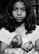 A young girl with medium-length hair is holding a few tomatoes in her hands. She has an expression of calm seriousness on her face and is wearing a T-shirt. The image is in black and white, providing a timeless and classic aesthetic.