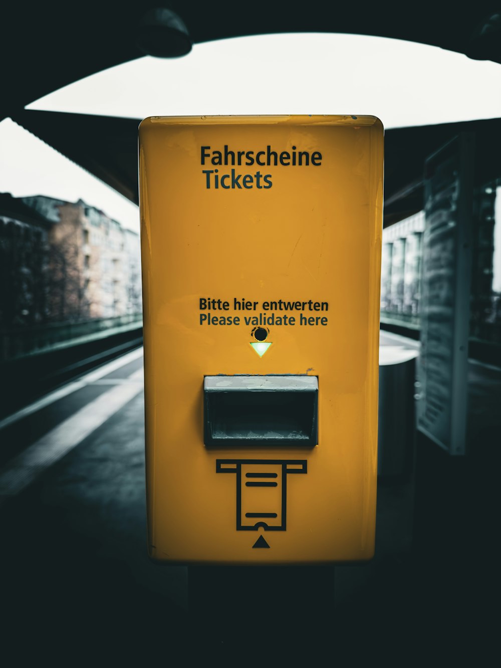 uma máquina de bilhetes amarela sentada ao lado de uma linha férrea