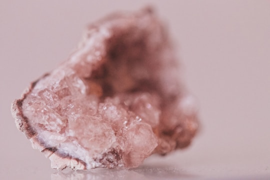 A close-up image of a rough, translucent pink mineral with crystalline structures. The stone's surface displays various facets and textures, with light reflecting off its shiny surfaces.