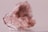 A close-up image of a rough, translucent pink mineral with crystalline structures. The stone's surface displays various facets and textures, with light reflecting off its shiny surfaces.