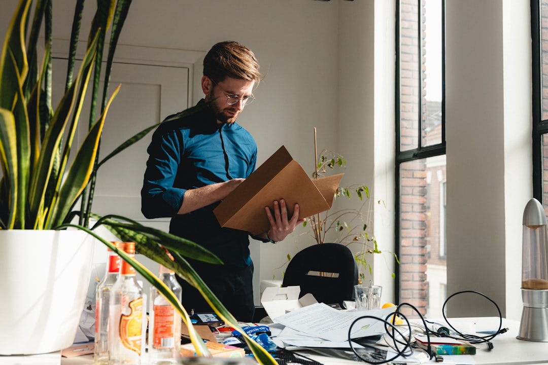 a man standing in an office holding a box, A man cleaning out a desk and looking through the final bookkeeping of a clos