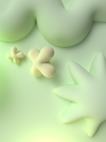 Soft, abstract shapes in pastel green and yellow tones are arranged on a smooth background. The forms are blobby, rounded, and create a calming visual effect.