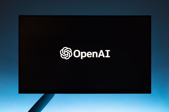 A black screen or display monitor with the OpenAI logo and text in white centered in the middle. The background is a gradient transitioning from dark to light blue from top to bottom.