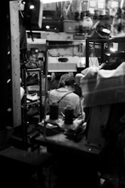 A tradesperson overwhelmed by paperwork and phone calls in a cluttered workshop.