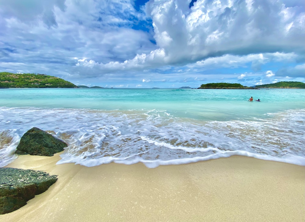 Ein Sandstrand mit ein paar Leuten im Wasser