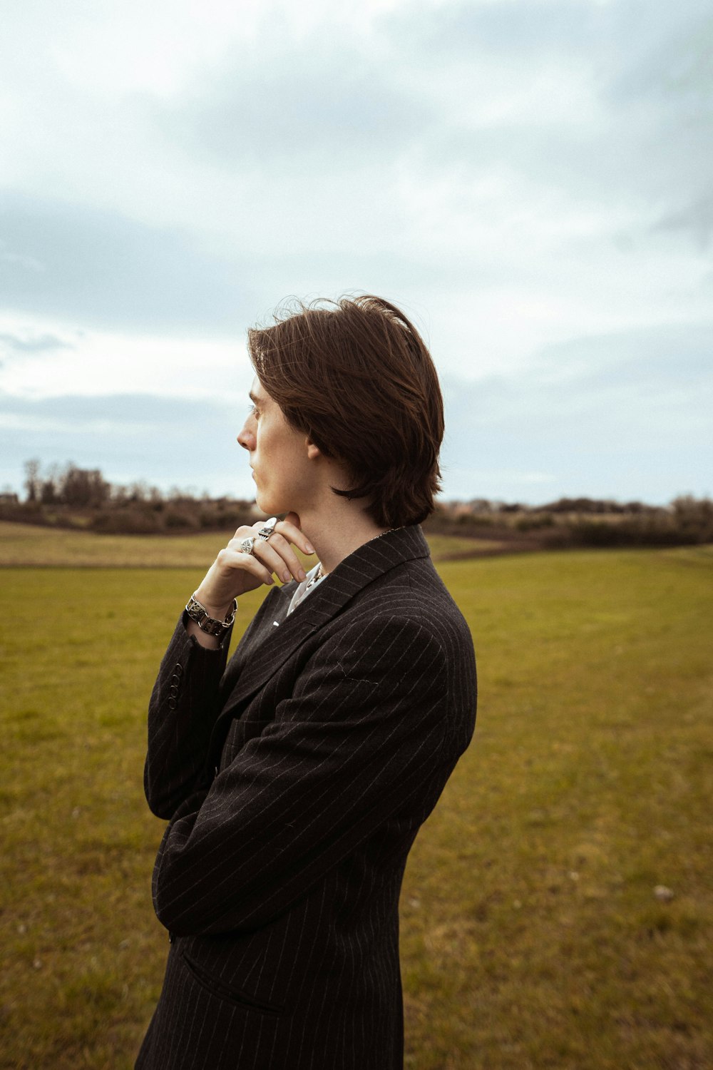 a woman standing in a field with her hand on her chin