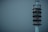 A tall, modern communication tower stands against a muted gray-blue sky. The structure is cylindrical with multiple levels, each adorned with various antennas and satellite dishes. Its sleek design and lights indicate it is active and operational.