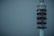 A tall, modern communication tower stands against a muted gray-blue sky. The structure is cylindrical with multiple levels, each adorned with various antennas and satellite dishes. Its sleek design and lights indicate it is active and operational.