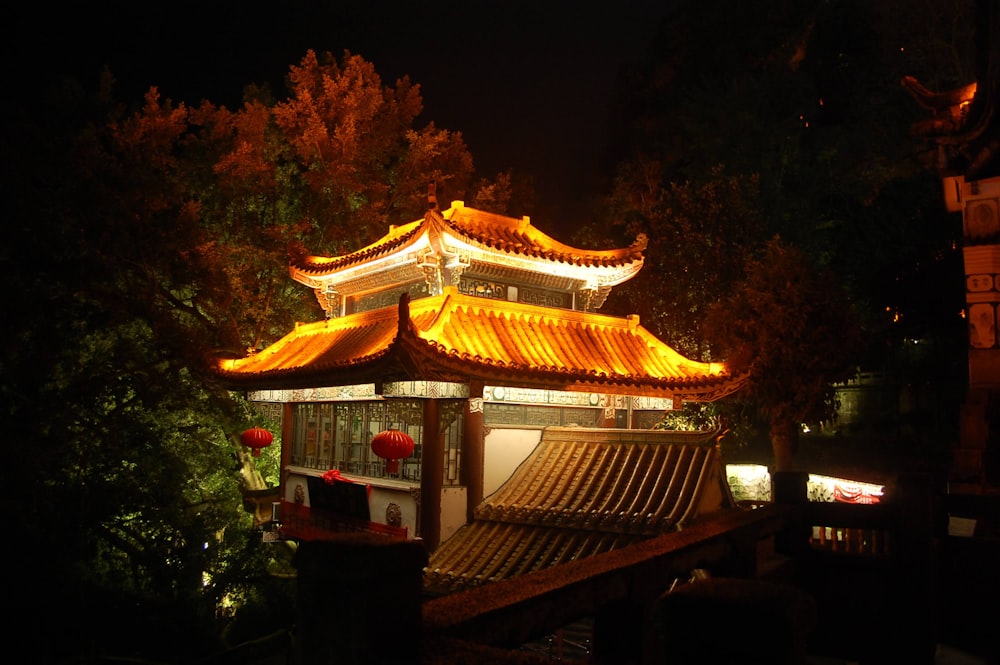 Un edificio chino iluminado por la noche con árboles en el fondo