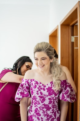 A smiling mother helping her daughter try on a delicate dress in a softly lit boutique.