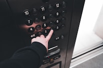 Close-up of a hand pressing an elevator button next to a bright media screen.