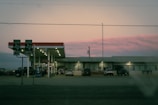 A gas station and convenience store, labeled 'Food Mart,' is situated at a crossroads. Several vehicles are parked near the pumps, and directional road signs indicate routes North and South for Highway 14. The sky displays a soft pink hue during what appears to be sunset or sunrise.