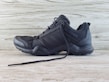 A black athletic shoe with a rugged sole and mesh detailing, designed for outdoor activities. It features brand markings on the side and is positioned against a light wooden background.