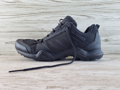 A black athletic shoe with a rugged sole and mesh detailing, designed for outdoor activities. It features brand markings on the side and is positioned against a light wooden background.