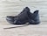 A black athletic shoe with a rugged sole and mesh detailing, designed for outdoor activities. It features brand markings on the side and is positioned against a light wooden background.