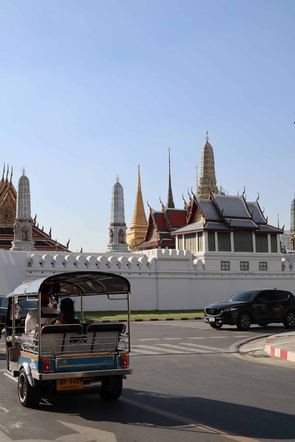 Un tuk tuk conduisant dans une rue devant un bâtiment blanc