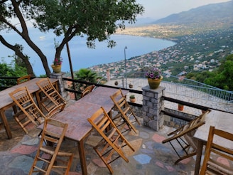 A cozy terrace with a dining set overlooking the Mediterranean coastline under a clear blue sky.