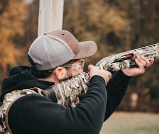 a man with a hat and glasses aims a rifle