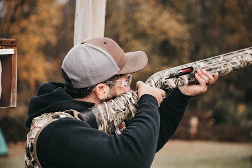 a man with a hat and glasses aims a shotgun