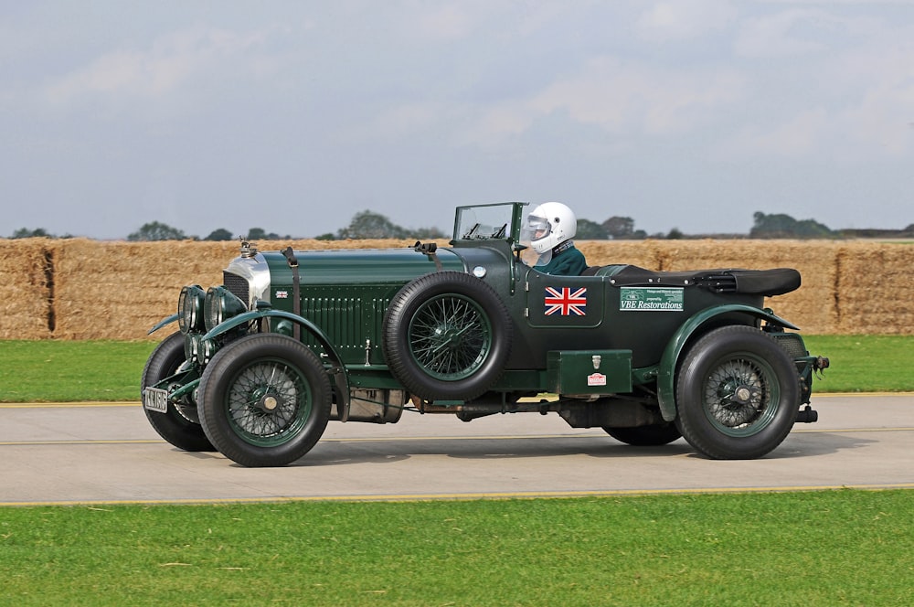 an old fashioned green car driving down a road