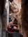 Four individuals are climbing through a narrow rocky crevice, with one person leading the way at a slightly higher altitude. The rocks are large and imposing, creating a sense of adventure and challenge.