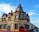 A traditional brick building with a combination of Victorian architectural elements, featuring red and beige tones. The upper part of the structure includes ornate detailing and a clock tower-like peak. Several signs advertise it as a bed and breakfast called 'The King Harry' with amenities such as a function room. The building is located on a street lined with similar row houses.