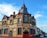 A traditional brick building with a combination of Victorian architectural elements, featuring red and beige tones. The upper part of the structure includes ornate detailing and a clock tower-like peak. Several signs advertise it as a bed and breakfast called 'The King Harry' with amenities such as a function room. The building is located on a street lined with similar row houses.