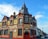 A traditional brick building with a combination of Victorian architectural elements, featuring red and beige tones. The upper part of the structure includes ornate detailing and a clock tower-like peak. Several signs advertise it as a bed and breakfast called 'The King Harry' with amenities such as a function room. The building is located on a street lined with similar row houses.