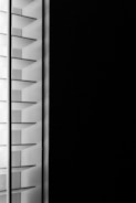 A close-up view of window blinds with horizontal slats, partially open, allowing minimal light to pass through against a dark background.