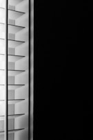 A close-up view of window blinds with horizontal slats, partially open, allowing minimal light to pass through against a dark background.