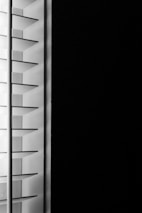 A close-up view of window blinds with horizontal slats, partially open, allowing minimal light to pass through against a dark background.