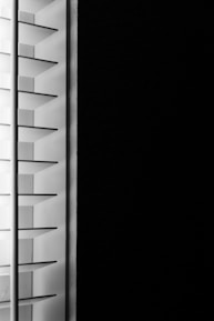 A close-up view of window blinds with horizontal slats, partially open, allowing minimal light to pass through against a dark background.