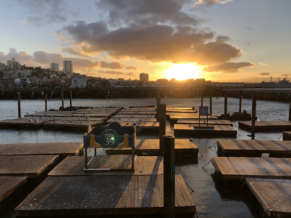 the sun is setting over a dock with wooden benches