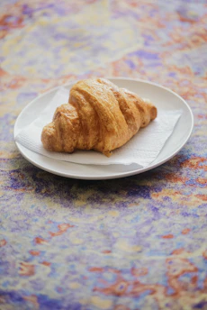 Golden croissant resting on a soft beige linen cloth with warm morning light.