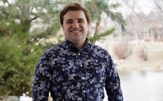 a man standing in front of a lake wearing a blue shirt